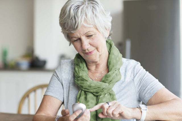 Senior woman using a mobile device while wearing a green scarf in a kitchen setting.
