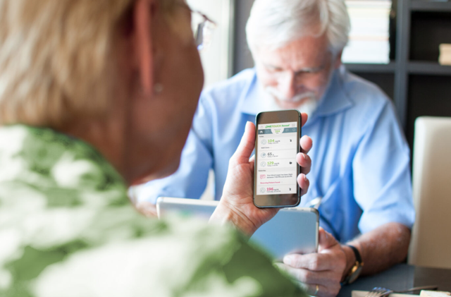Elderly woman holding a smartphone displaying health data during a consultation.