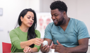 Healthcare professional discussing medication with a patient in a clinical environment.