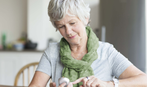 Senior woman using a mobile device while wearing a green scarf in a kitchen setting.