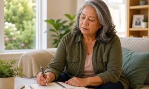 Woman writing notes in a journal at home while sitting on a couch