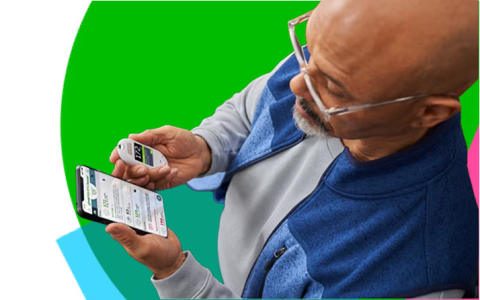 Older man looking at a smartphone and a handheld medical device against a colorful background.